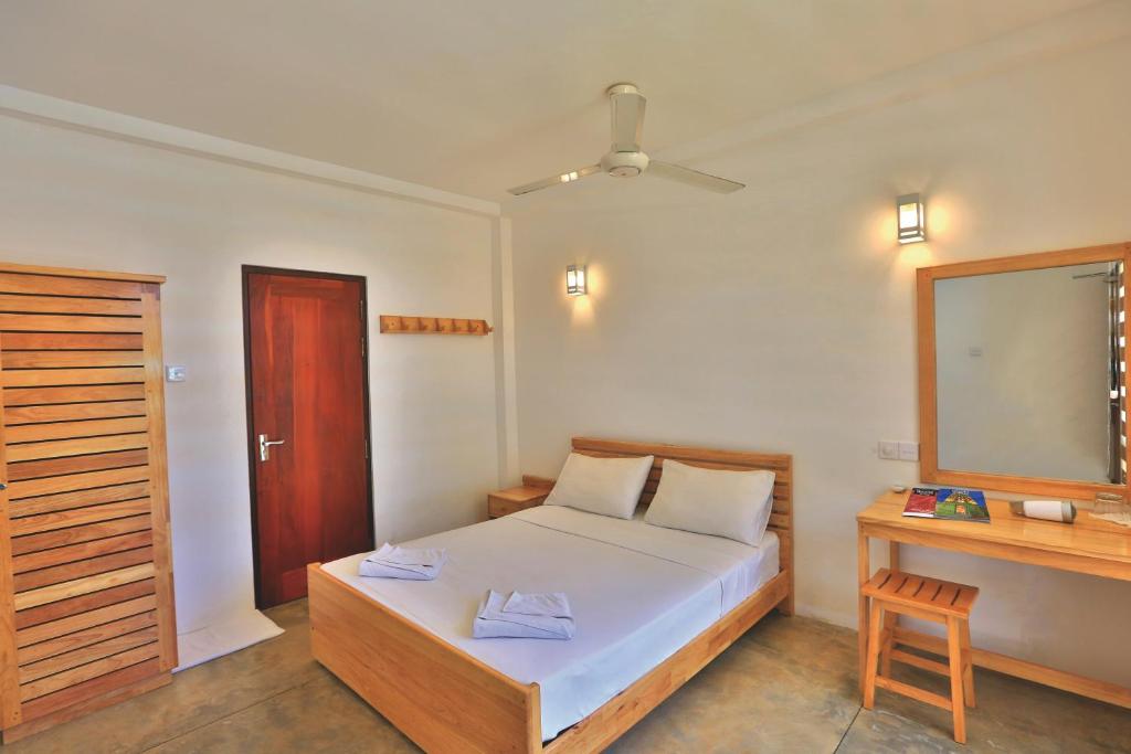 a bedroom with a bed and a desk and a mirror at Arugambay Roccos in Arugam Bay