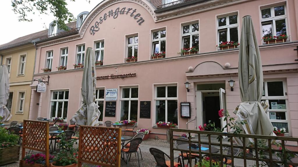 ein rosafarbenes Gebäude mit geschlossenen Sonnenschirmen davor in der Unterkunft Restaurant Rosengarten in Neuruppin
