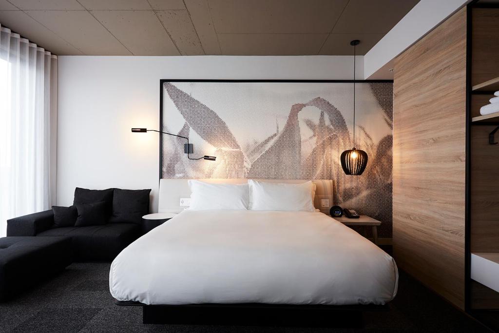 a bedroom with a large white bed and a couch at Hôtel Escad Quartier DIX30 in Brossard