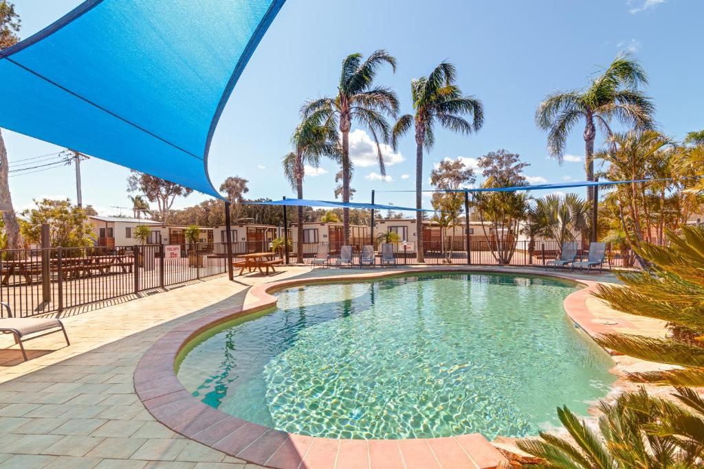 una piscina con ombrellone blu e palme di Birubi Beach Holiday Park ad Anna Bay