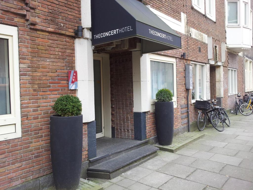 une porte d'entrée d'un bâtiment en briques avec deux plantes en pot dans l'établissement The Concert Hotel, à Amsterdam