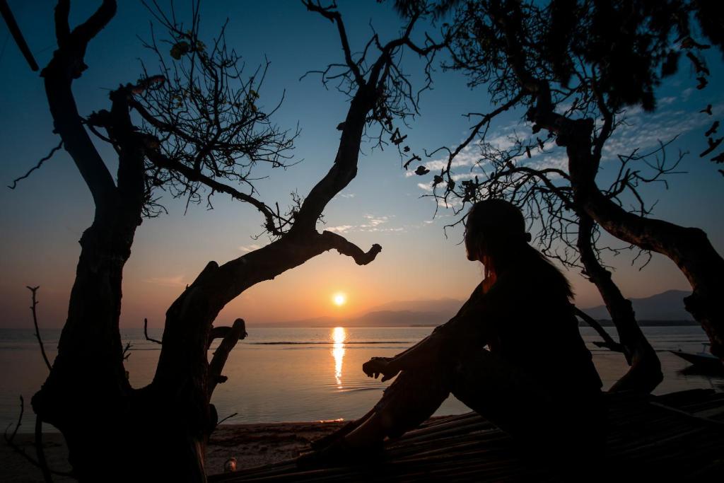 a woman sitting on a bench on the beach watching the sunset at Abdi Fantastik in Gili Islands