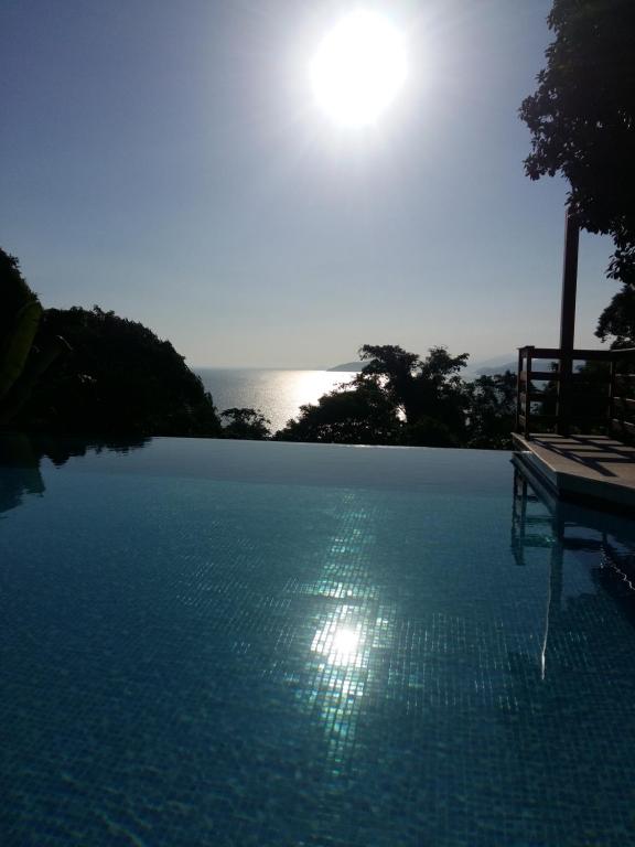 a large swimming pool with the sun in the background at ILHABELA PRAIA DO CURRAL Condômino VilaBela da Princesa in Ilhabela