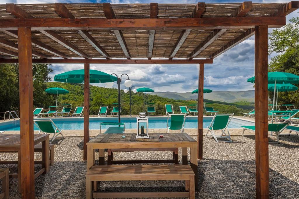 a wooden pergola with a table and chairs next to a pool at Tenuta della Selva in Monteroni dʼArbia