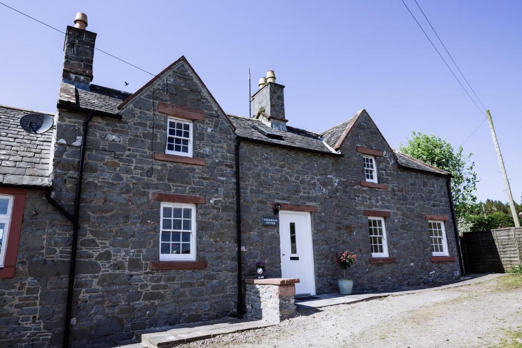 uma antiga casa de pedra com portas e janelas brancas em Stockman's Cottage em Kirkcudbright