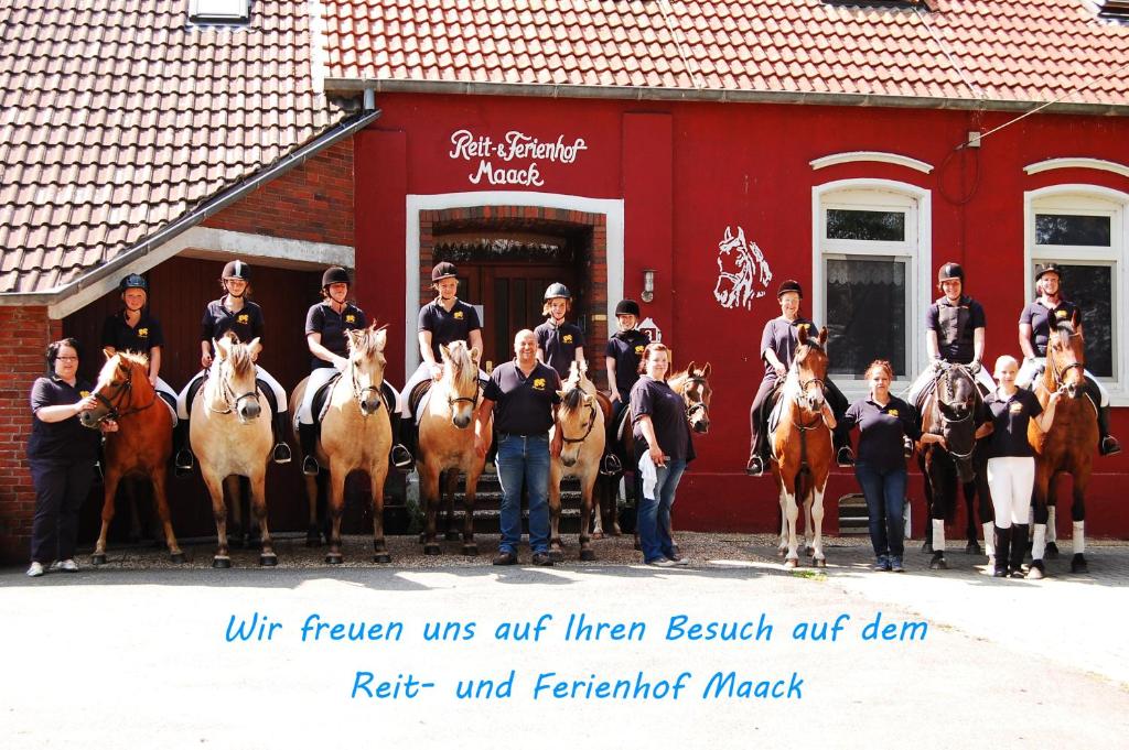 eine Gruppe von Menschen und Pferden vor einem roten Gebäude in der Unterkunft Reit- und Ferienhof Maack in Neuharlingersiel