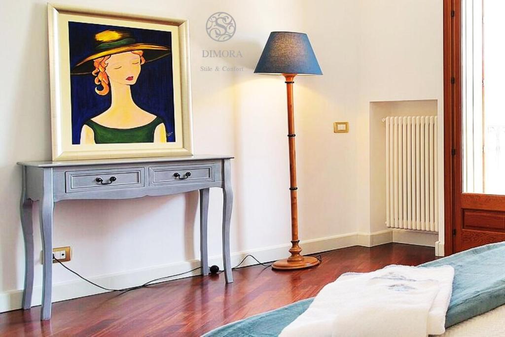 Ein Gemälde einer Frau auf einem Tisch neben einer Lampe in der Unterkunft DIMORA Annetta in Ispica
