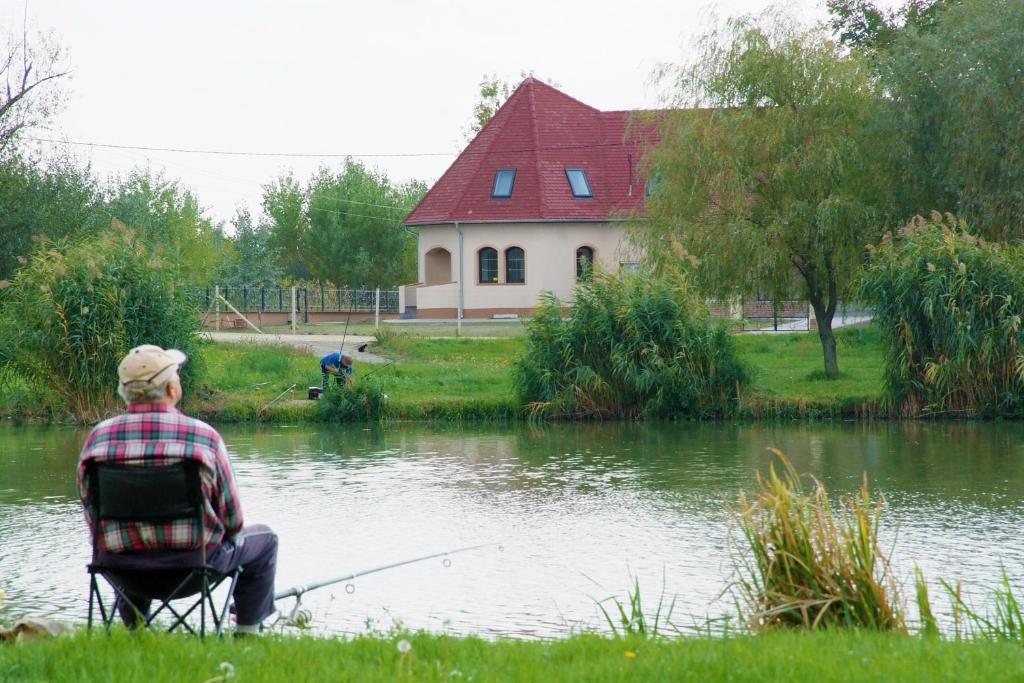 un hombre sentado en una silla pescando en un lago en Tiszavilág Pihenőház en Tiszakécske