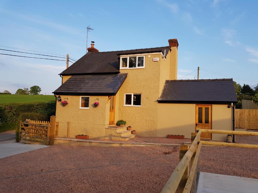 une maison jaune avec un toit noir et une clôture dans l'établissement yew tree cottage, à Hereford