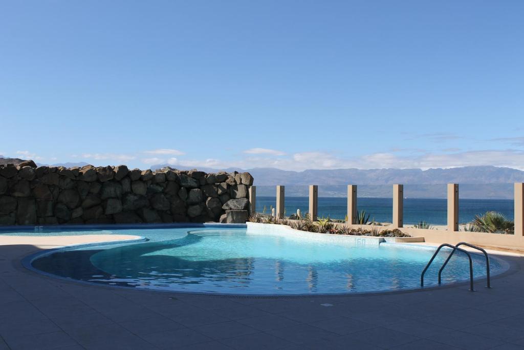 a swimming pool with a stone wall and the ocean at Apartamento Las Rochas in Mindelo