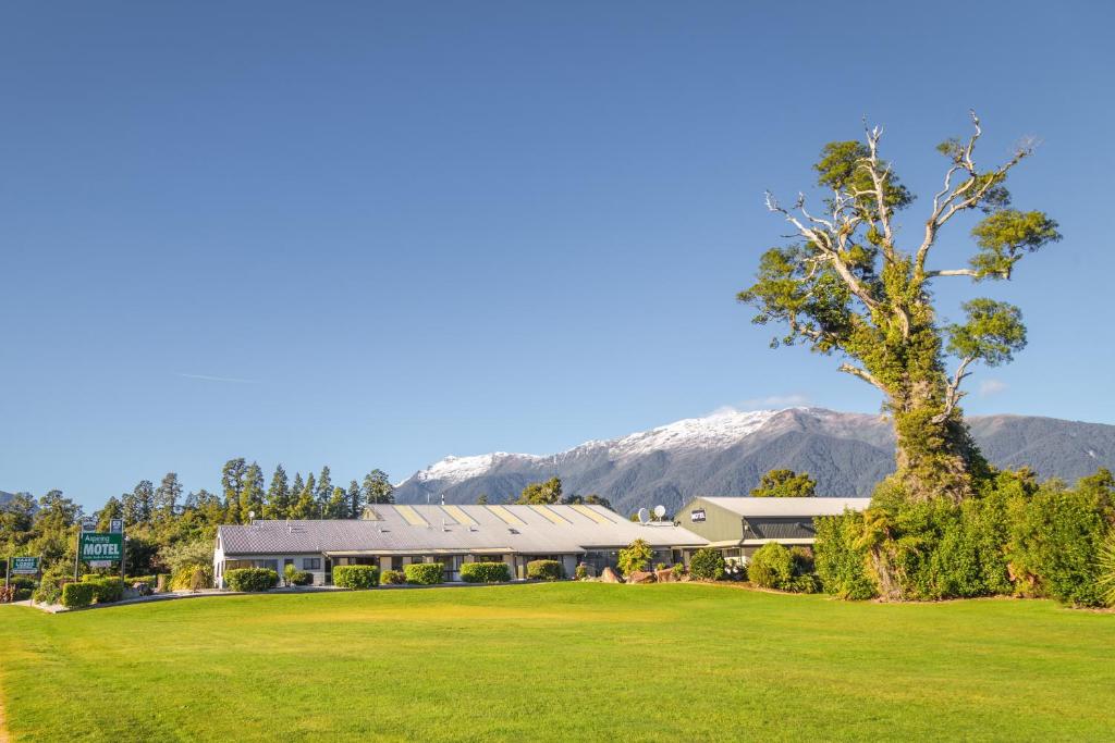 um grande edifício com um campo verde e montanhas ao fundo em ASURE Aspiring Court Motel em Haast