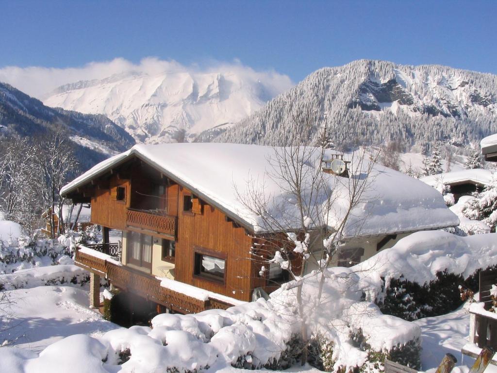 a cabin covered in snow with mountains in the background at Chalet La Licorne au pied des pistes in Notre-Dame-de-Bellecombe