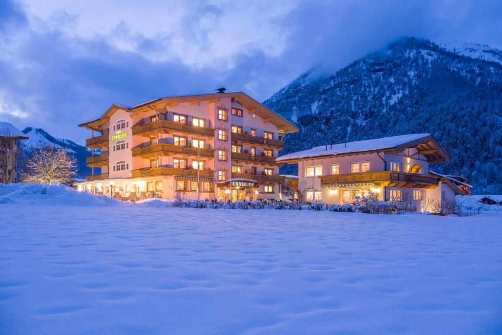 a large building in the snow in front of a mountain at Liebes Caroline 4-Sterne-Hotel in Pertisau