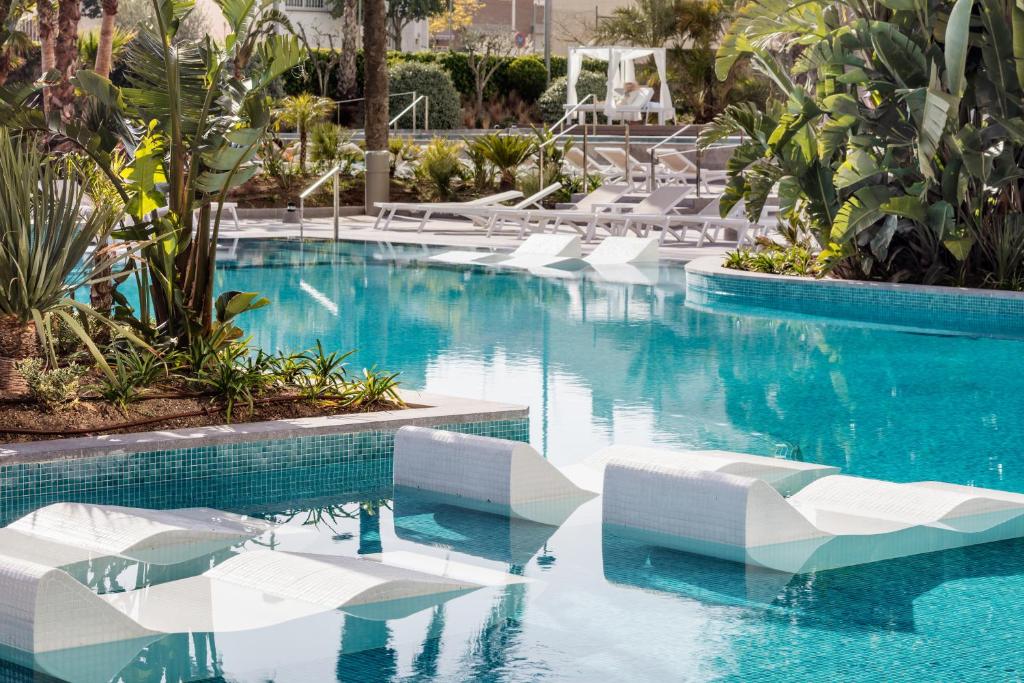 - une piscine avec des chaises blanches et de l'eau bleue dans l'établissement AQUA Hotel Silhouette & Spa - Adults Only, à Malgrat de Mar