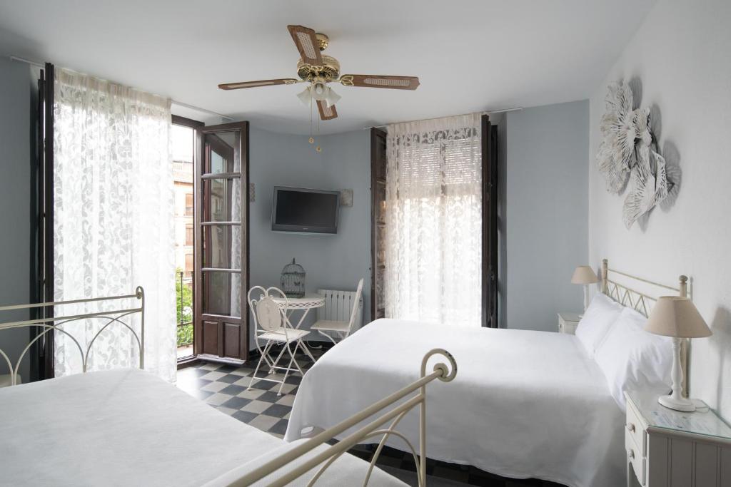 a white bedroom with two beds and a tv at Pension Venecia Gomerez in Granada