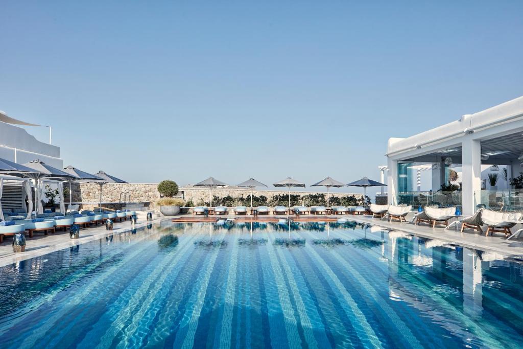 a large swimming pool with chairs and umbrellas at Myconian Kyma, a Member of Design Hotels in Mýkonos City