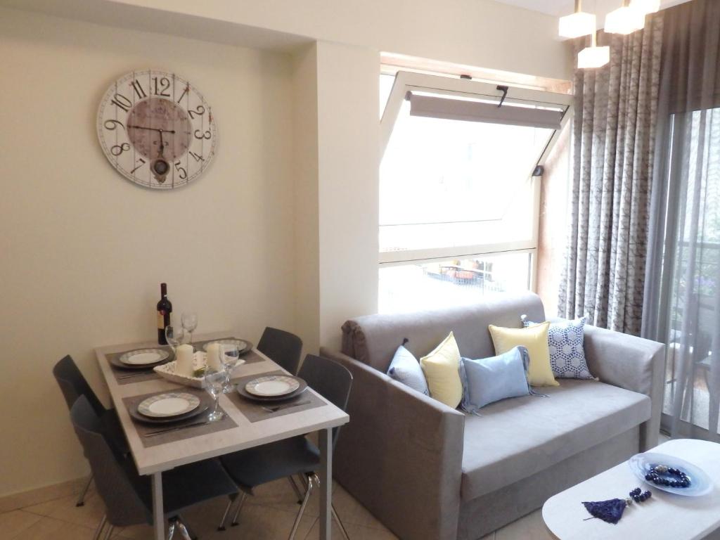 a living room with a table and a couch and a clock at Lion Apartment Sunset in Thessaloniki