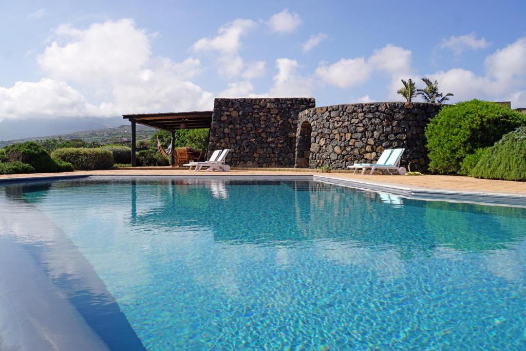 a large swimming pool with two chairs and a building at Dammusi I Jardina in Pantelleria