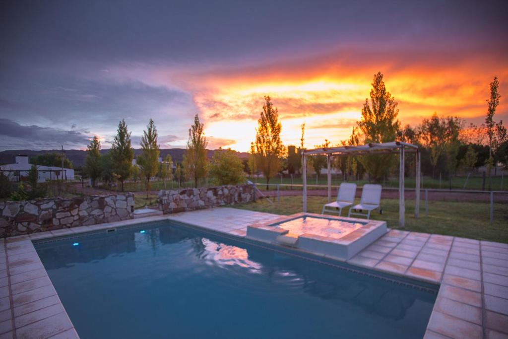 a swimming pool with two chairs and a sunset at La Agustina Complejo Apart in Valle Grande