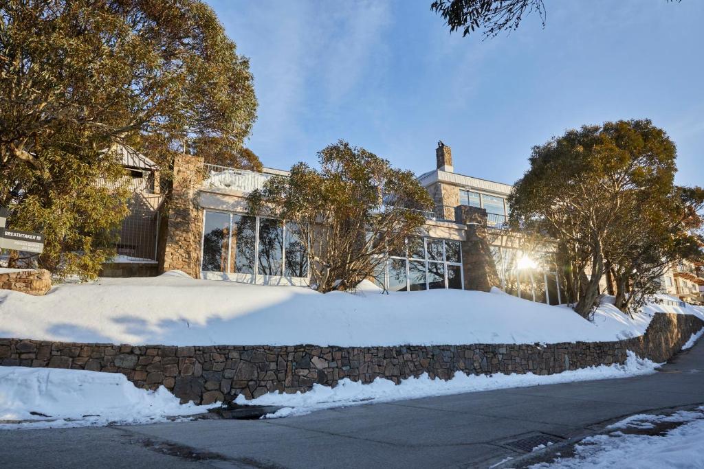 a house with a stone wall in the snow at Breathtaker Hotel and Spa in Mount Buller