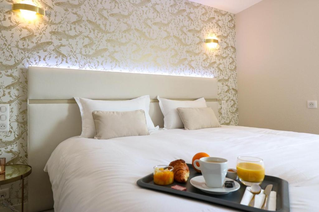 a tray of food on a bed with orange juice at Hotel l'Ortega Rennes Aeroport in Saint-Jacques-de-la-Lande