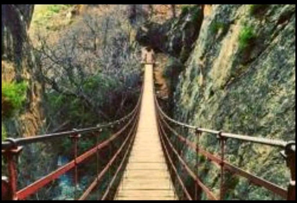 un ponte sospeso sopra un canyon con una montagna di La Casita de Gonzalo a Monachil