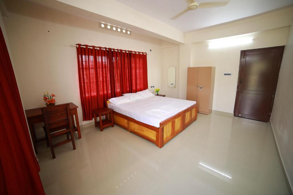 a bedroom with a bed and a desk and red curtains at Indeevaram Residency in Trivandrum