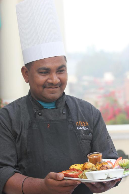 a man wearing a chef hat holding a plate of food at Hotel Surya, Kaiser Palace in Varanasi