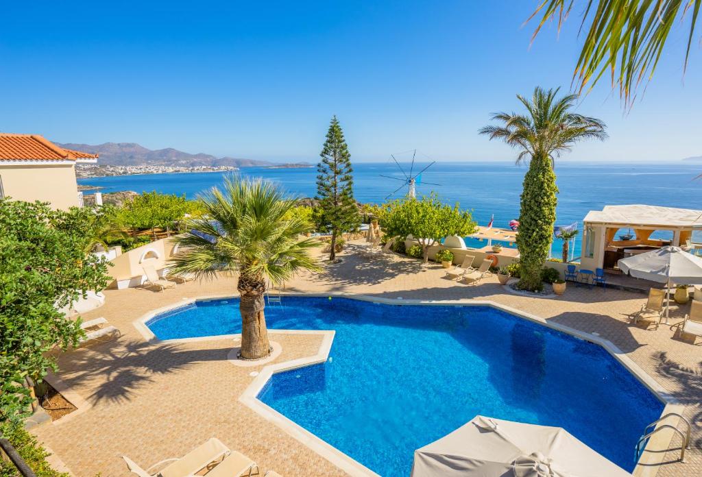 einen Pool mit Palmen und dem Meer im Hintergrund in der Unterkunft Panorama Villas - Adults Only in Agios Nikolaos