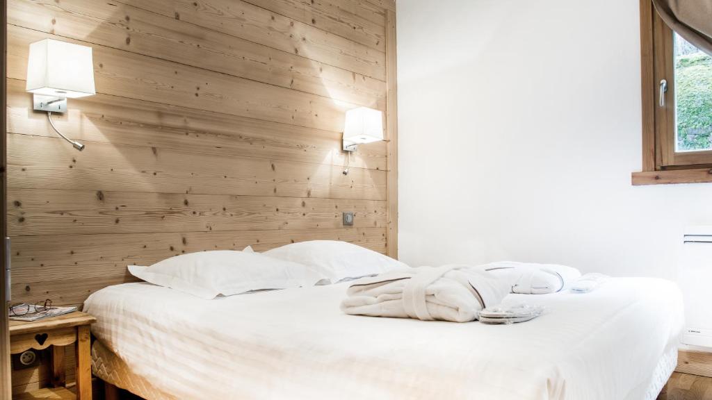 a bedroom with a white bed with a wooden wall at Résidence - Les Grandes Alpes in La Clusaz