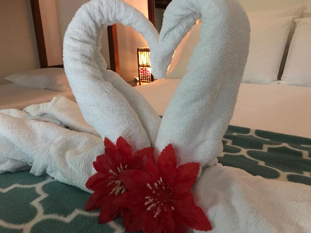 a couple of towels on a bed with a red flower at Pousada do Mineiro in Trancoso