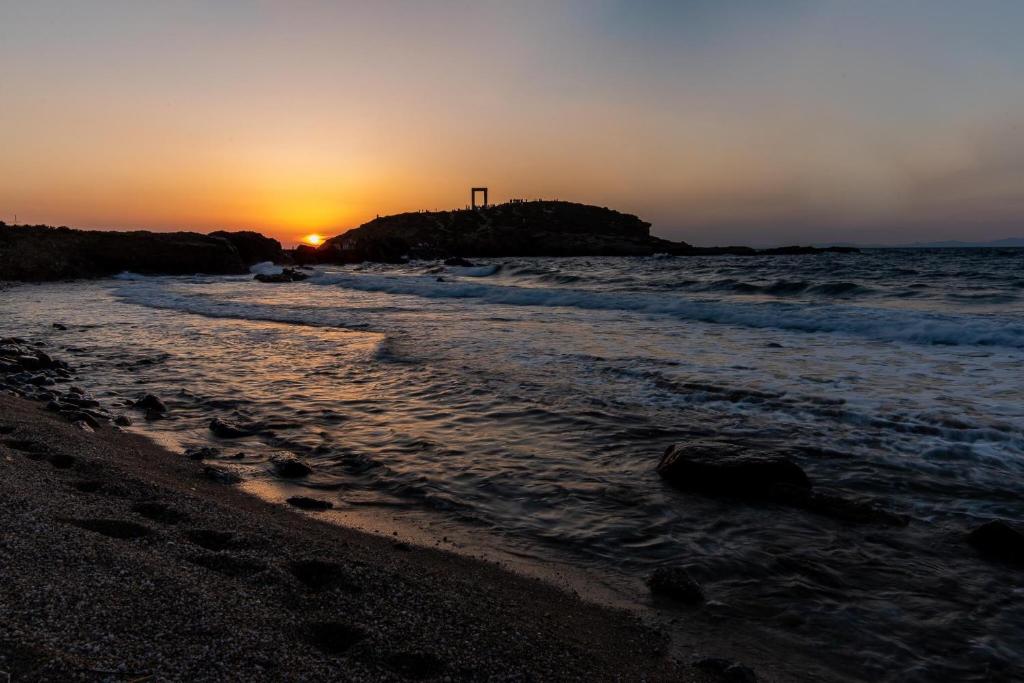 the sun is setting on the beach near the ocean at Portara Seaside Luxury Suites in Naxos Chora