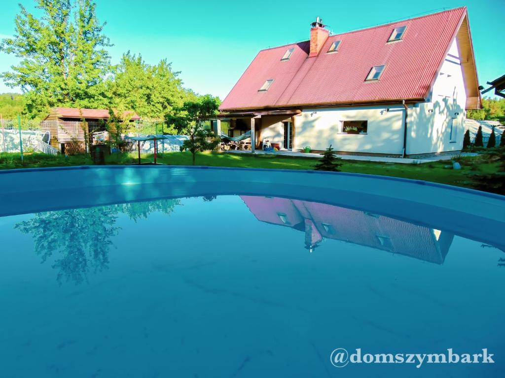 ein Haus mit rotem Dach und einer Reflexion im Wasser in der Unterkunft Dom caloroczny w Szymbarku in Szymbark