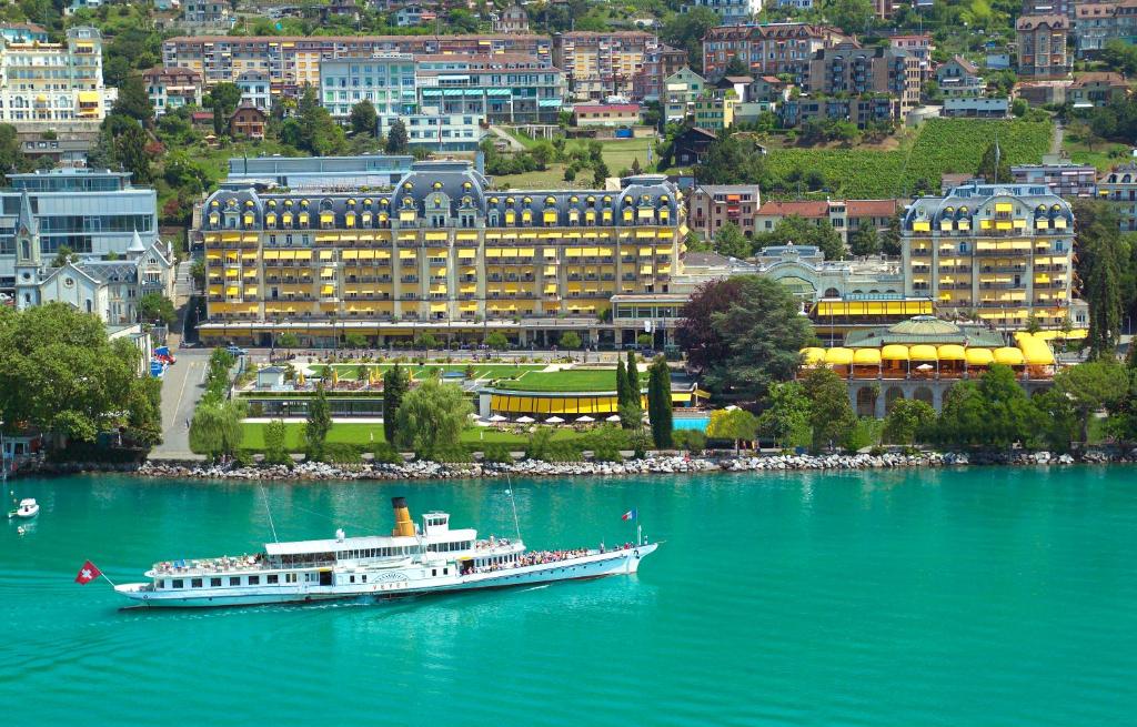 a boat in the water in front of a city at Fairmont Le Montreux Palace in Montreux