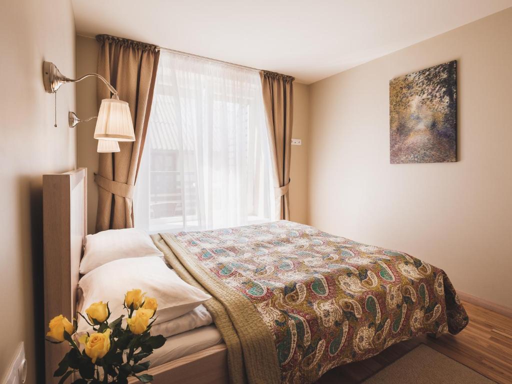 a bedroom with a bed with a window and a vase of flowers at Palangos Vila Apartments in Palanga