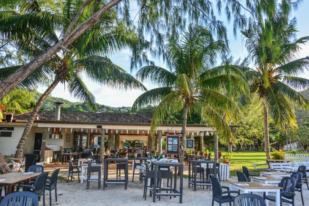 a restaurant with tables and chairs and palm trees at Berjaya Praslin Resort in Anse Volbert Village