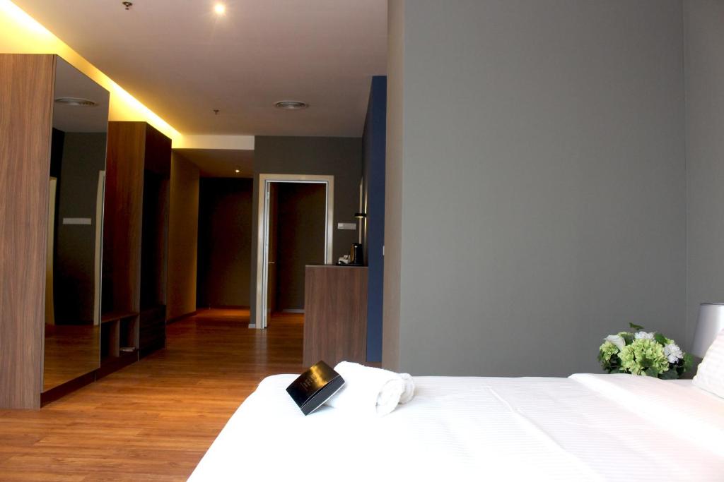A bedroom corner with a white bed, mirrored storage and a long wood-floored entry.