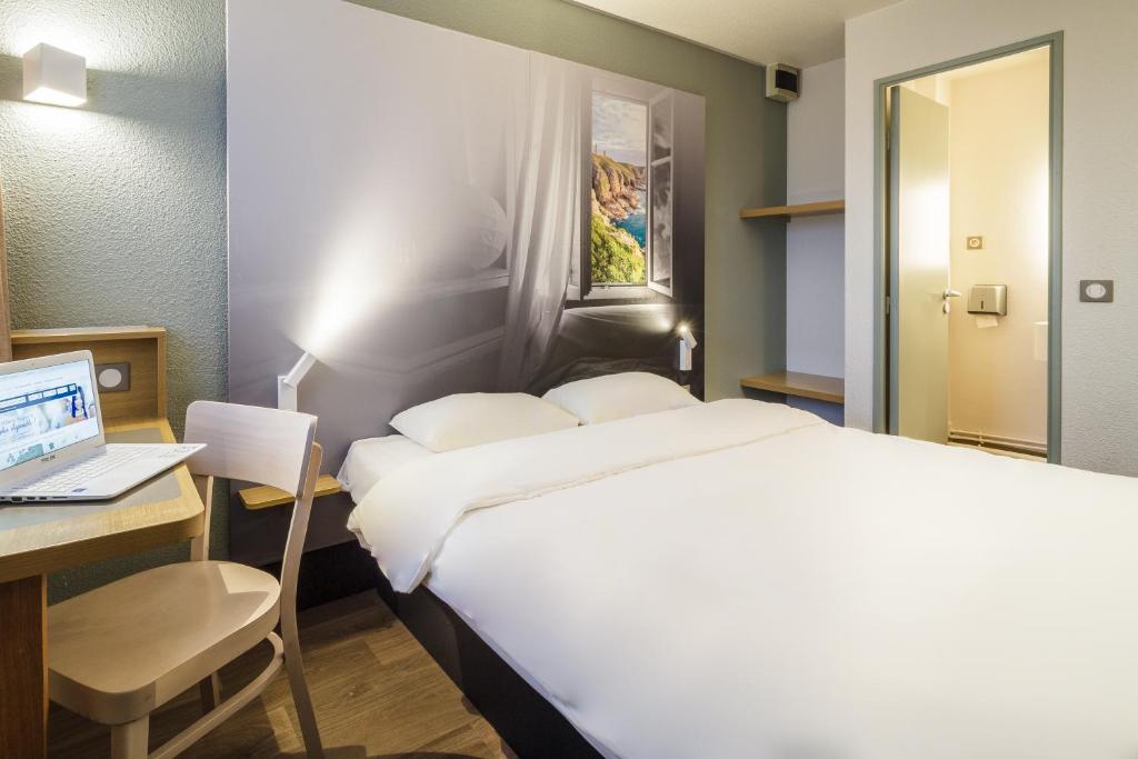 a bedroom with a bed and a desk with a laptop at B&B HOTEL Saint-Brieuc in Tregueux