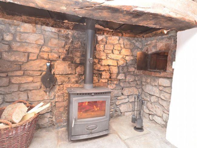 a stone wall with a stove in a room at Red Rose Cottage in Cheddar