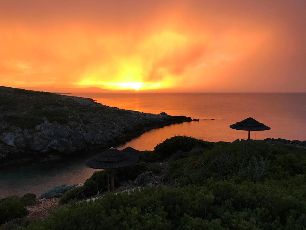 a sunset over the ocean with umbrellas on a beach at Giorgi's Blue Apartments in Kalathas