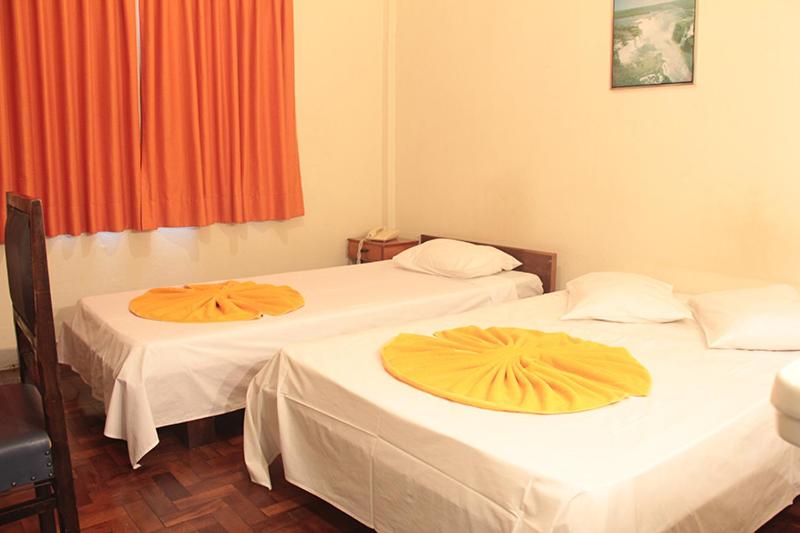 two beds in a room with orange curtains at Hotel Indaiá in Maringá