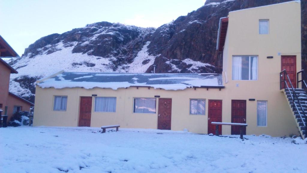 a building with snow on the roof in front of a mountain at Milenarios Hostel in El Chalten