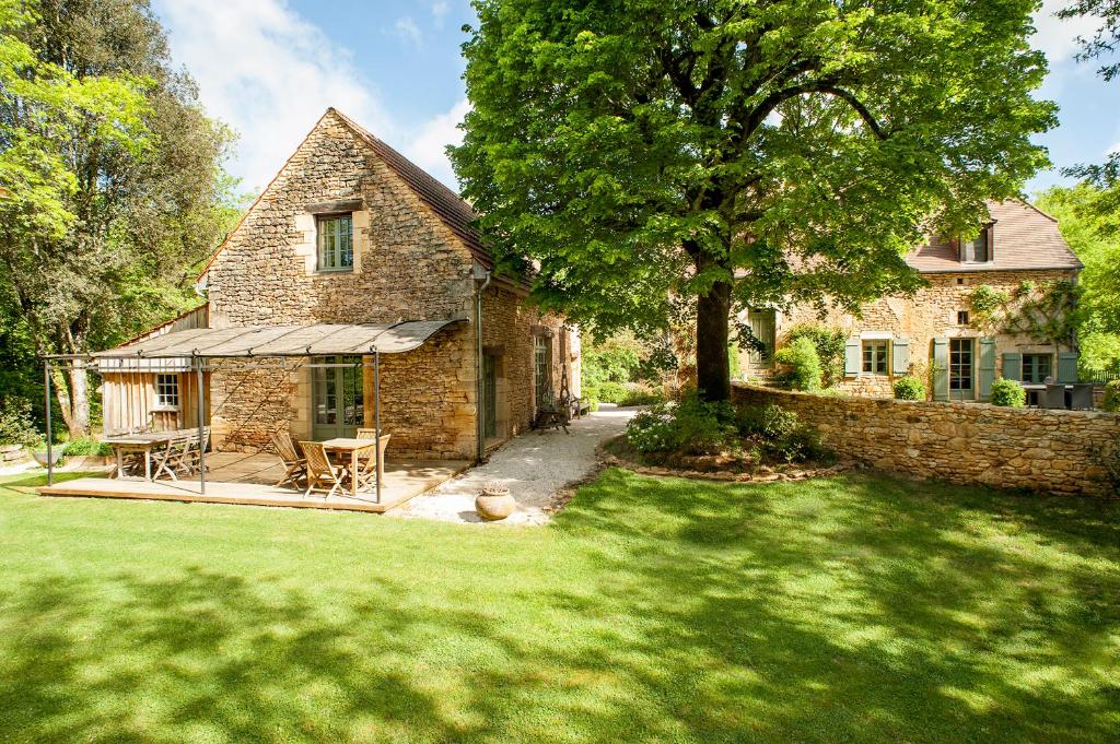 a stone house with a table and chairs in a yard at La Closerie De Sarlat in Sainte-Nathalène