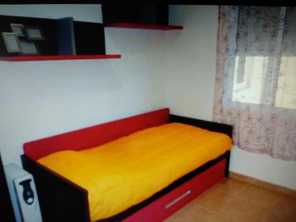 a red and yellow bed in a room with a window at VIVIENDA TURISTICA MARANt 2 in El Puerto de Santa María