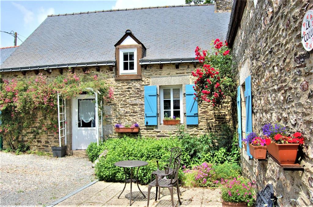 een stenen huis met een tafel en stoelen ervoor bij Coet Moru Gites - Rose Cottage in Crédin