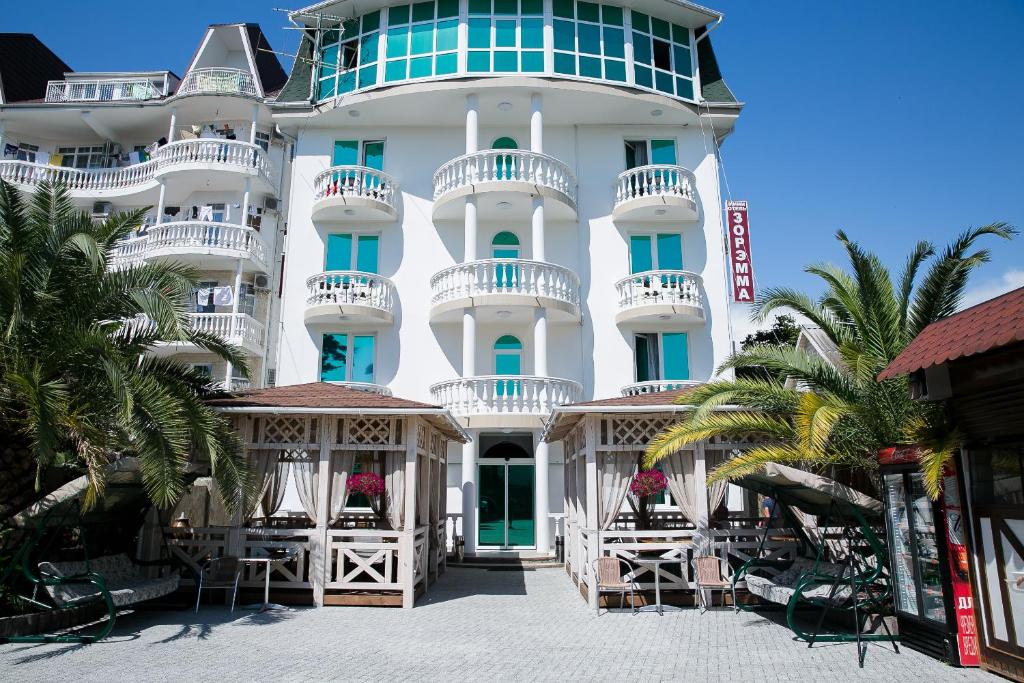a large white building with white balconies and palm trees at Zoremma Mini-hotel in Adler