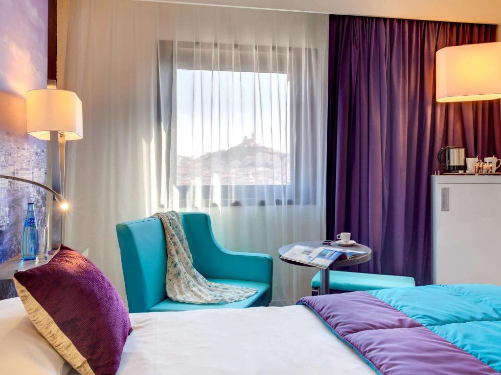 
a hotel room with a bed, chair, lamp and window at Mercure Marseille Centre Vieux Port in Marseille
