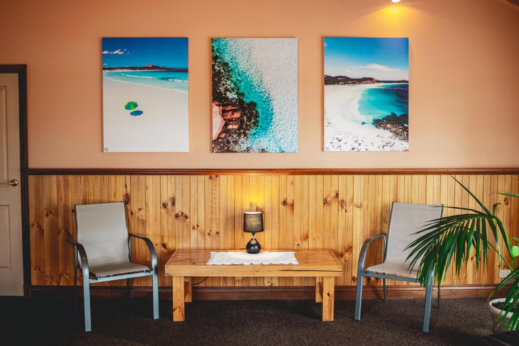 a room with three chairs and a wooden table and a table and three paintings at Esperance Foreshore Apartments in Esperance