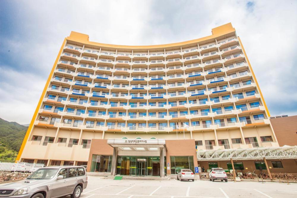 Jiri Mountain Ilsung Condo في Namwon: مبنى كبير فيه سيارات تقف امامه