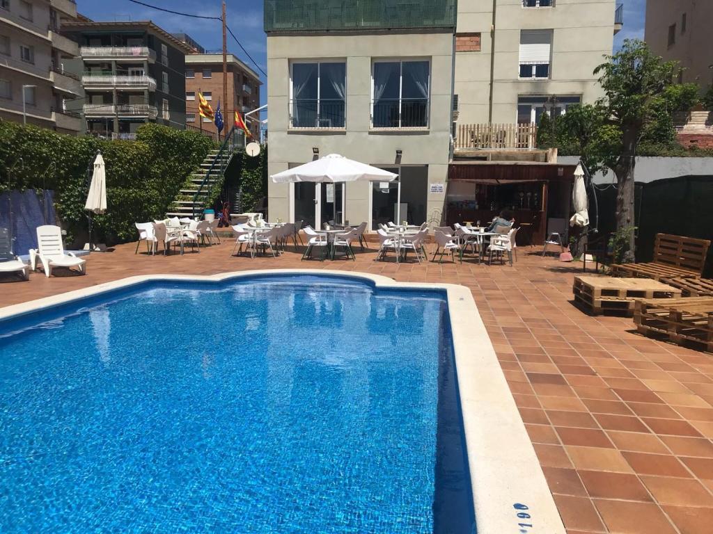 a swimming pool with chairs and tables and a building at Hotel Sant Jordi in Segur de Calafell